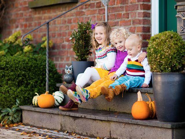 children sitting on the steps of a house with pumpkins 