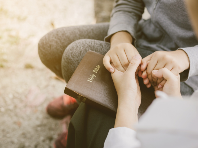 holding hands with a Bible nearby and praying
