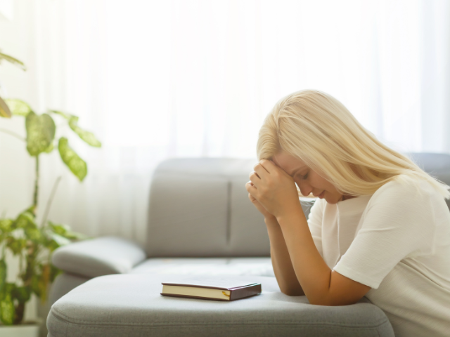 young woman praying at a coffee table with a Bible on it