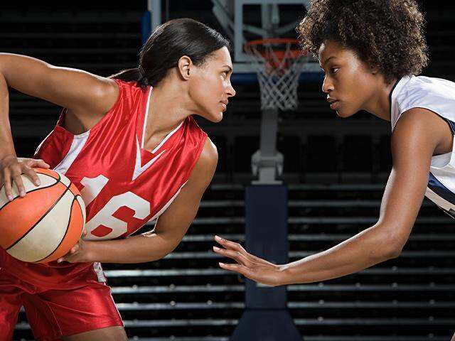 two young women playing basketball in uniforms