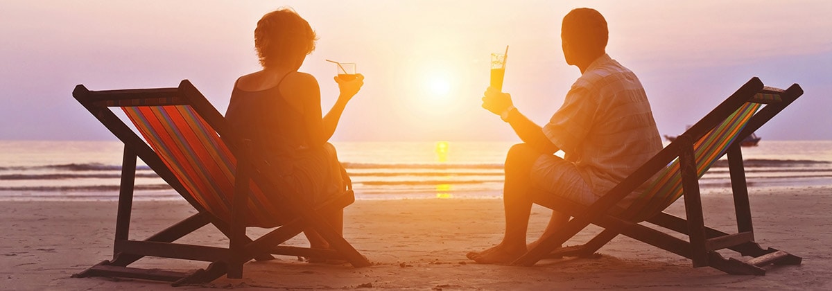 man and woman enjoying a relaxing vacation with drinks on the beach at sunset