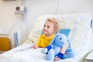 Boy with stuffed animal sits up in hospital bed