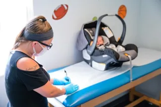 Baby in car seat sits on exam table as clinician prepares for appointment