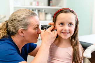 smiling girl getting her ear examined by a pediatrician