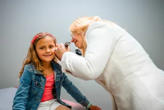 a girl smiling at the camera as she gets her ear examined by a female pediatrician