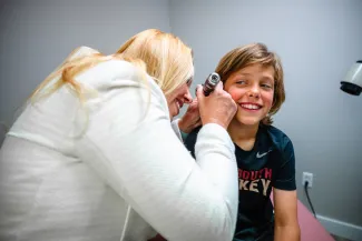 a boy smiling while a female pediatrician looks in his ear