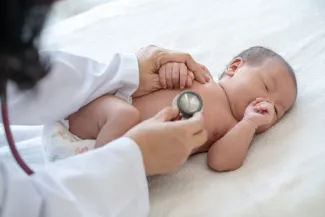 a newborn baby asleep while a pediatrician using a stethoscope on their chest