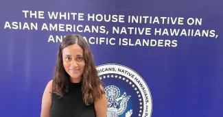 Conference attendee with backdrop: Writing says: The White House Initiative on Asian Americans, Native Hawaiians, and Pacific Islanders