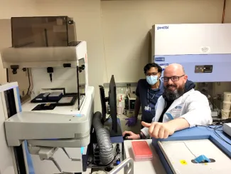 two men in a lab sitting next to a white ArrayScan™ XTI machine