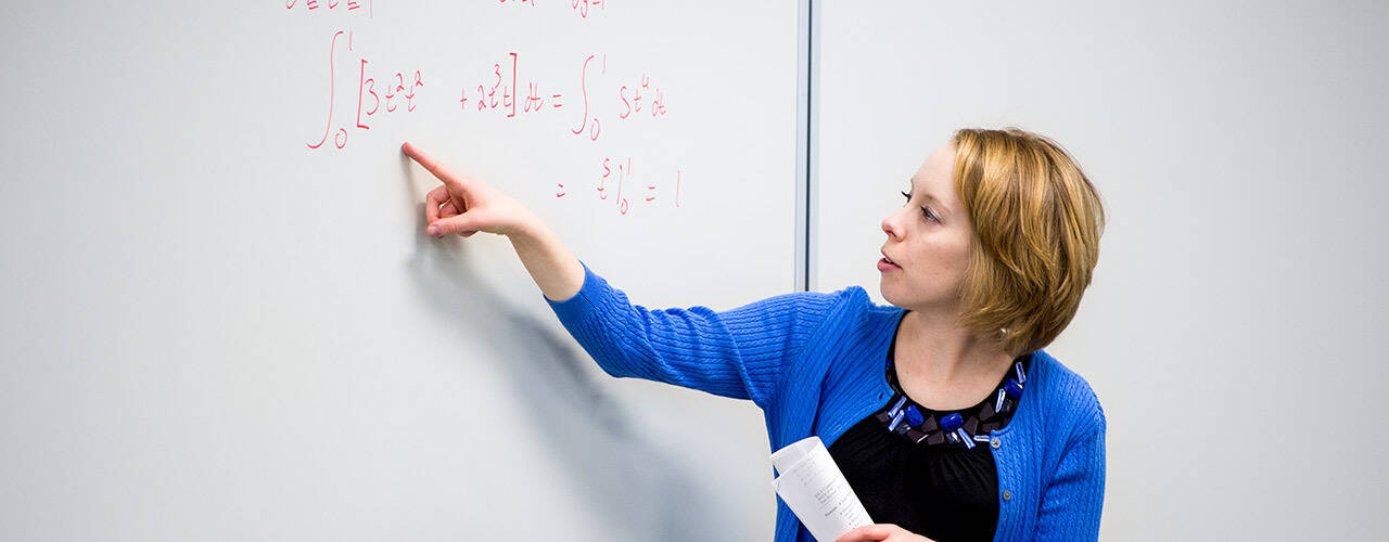 Cedarville University math professor pointing at a math question on a white board