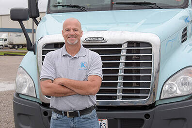 Keller Trucking professional driver, Carl Dotson, standing in front of his semi truck with arms crossed 