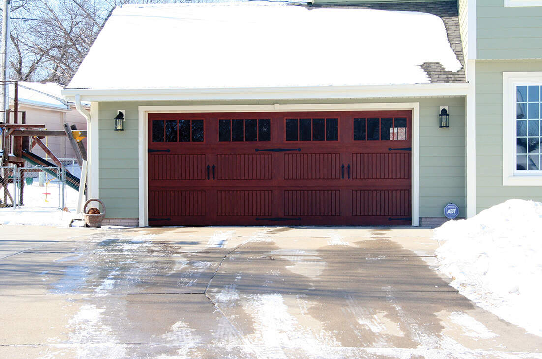 Two-car maroon garage door with snow-covered roof and icy driveway