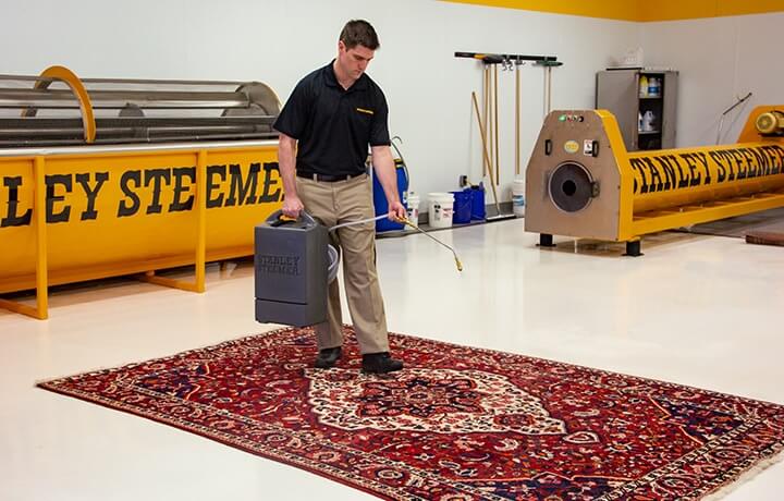 Stanley Steemer technician spraying rug protector on an oriental area rug.