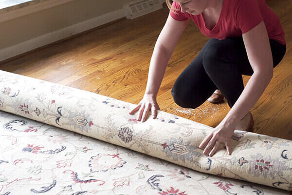 Woman moving rug to clean hardwood