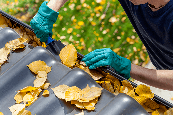 Man cleaning gutters and removing leaves with shovel