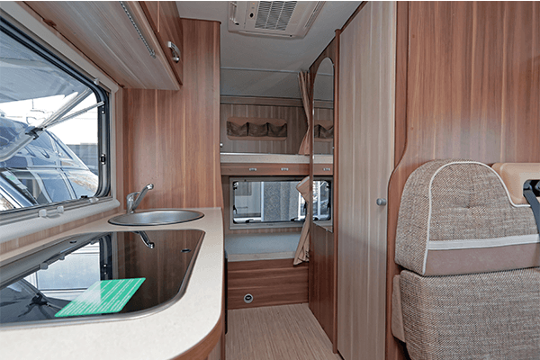 RV living space showing the kitchenette to the side and seating. Wood paneling are the walls.