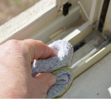 Hand cleaning the dirty tracks of a window with a towel. 