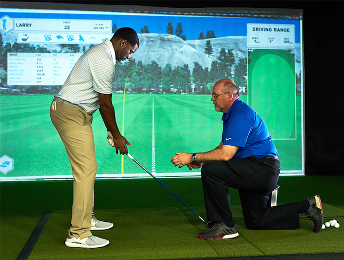 A man standing with a golf club in front of a projector screen receives lessons from an employee at PGA TOUR Superstore in Northeast Florida.
