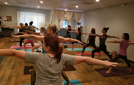 A group of yogis in warrior pose during a yoga class hosted by Emerald Yoga Studio.