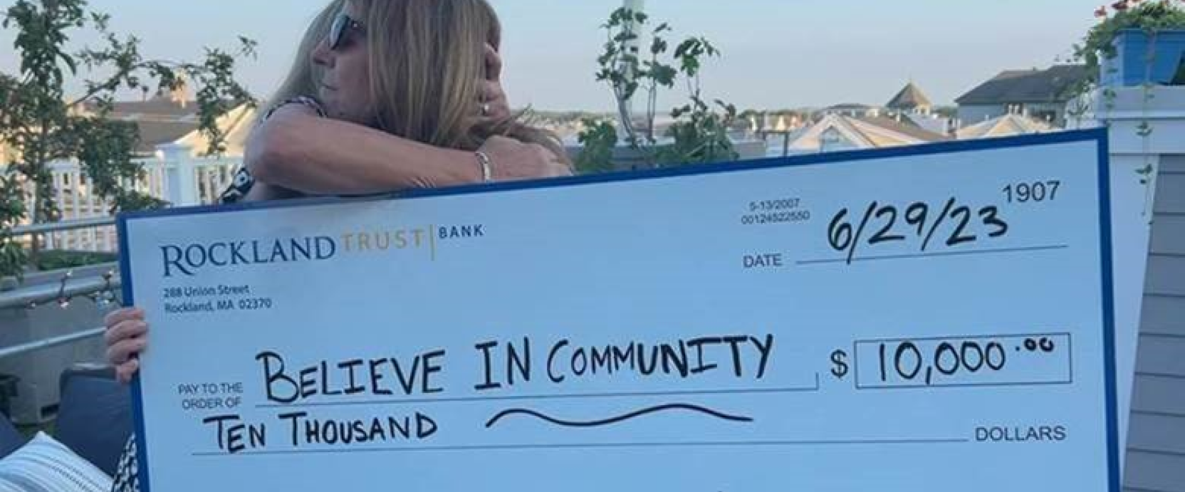 Two women from "Believe in Community" hugging to celebrate a check of 10,000 dollars from Rockland Trust's Charitable Giving Foundation.