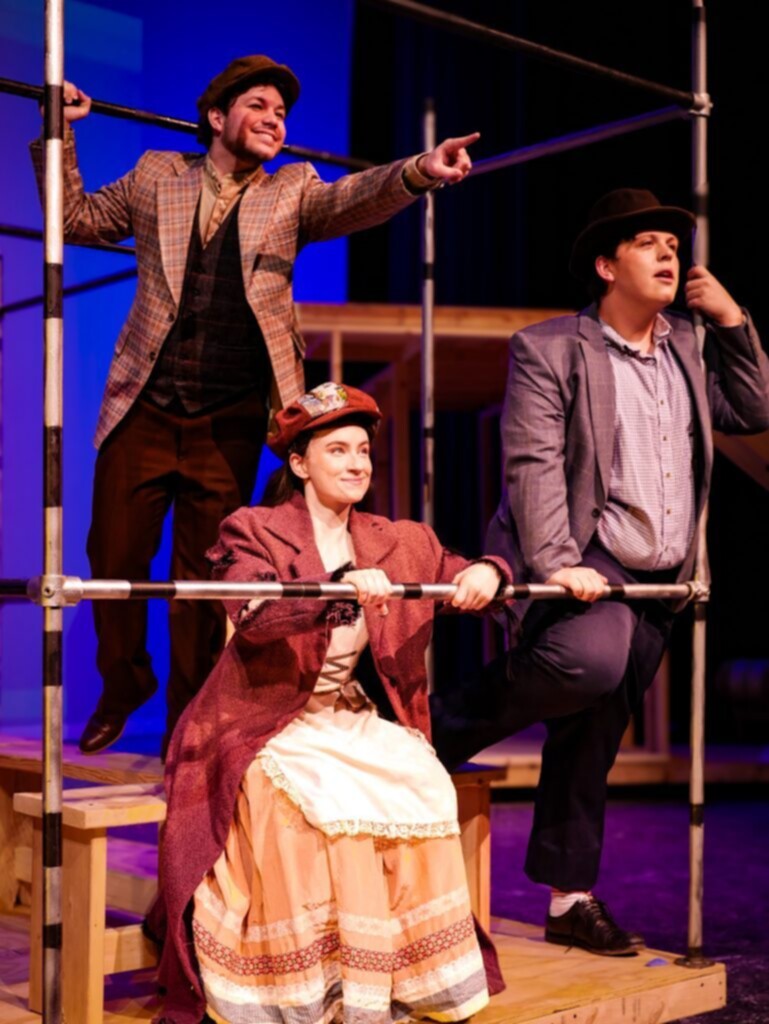 Valparaiso University students perform on stage during a rehearsal for a theatrical production, dressed in period costumes and engaging with the set in a dramatic scene.