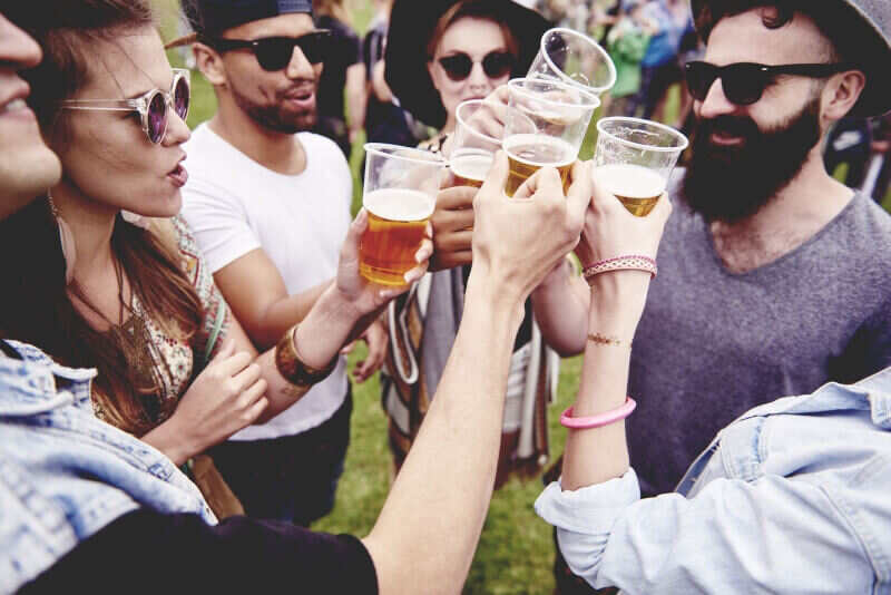A small group of people at a festival bring plastic cups of beer together in celebration.