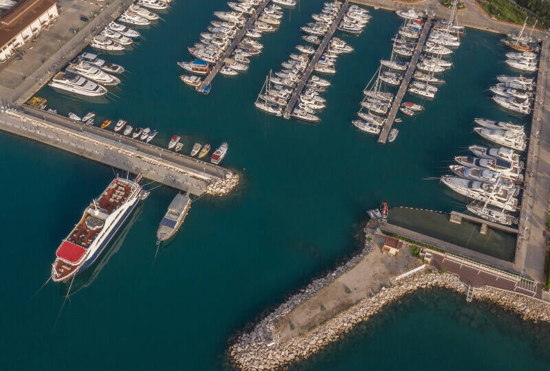 A marina pictured from above. Dozens of small boats are docked in the marina, as well as a larger boat docked along the outer edge.