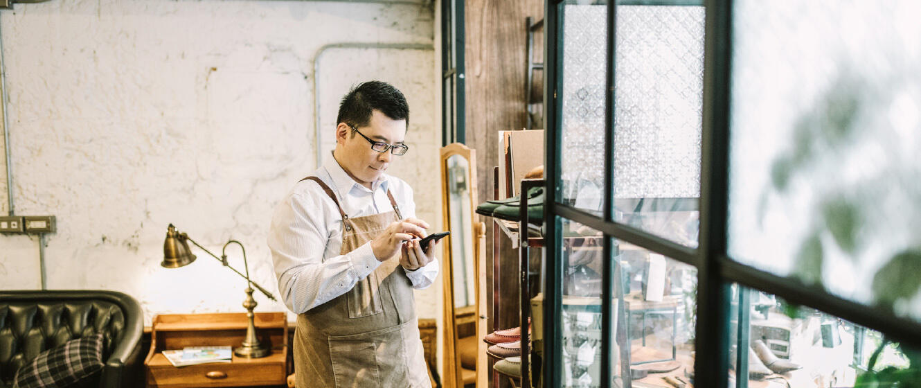 Small Business owner in his shop with apron on while looking on his smartphone