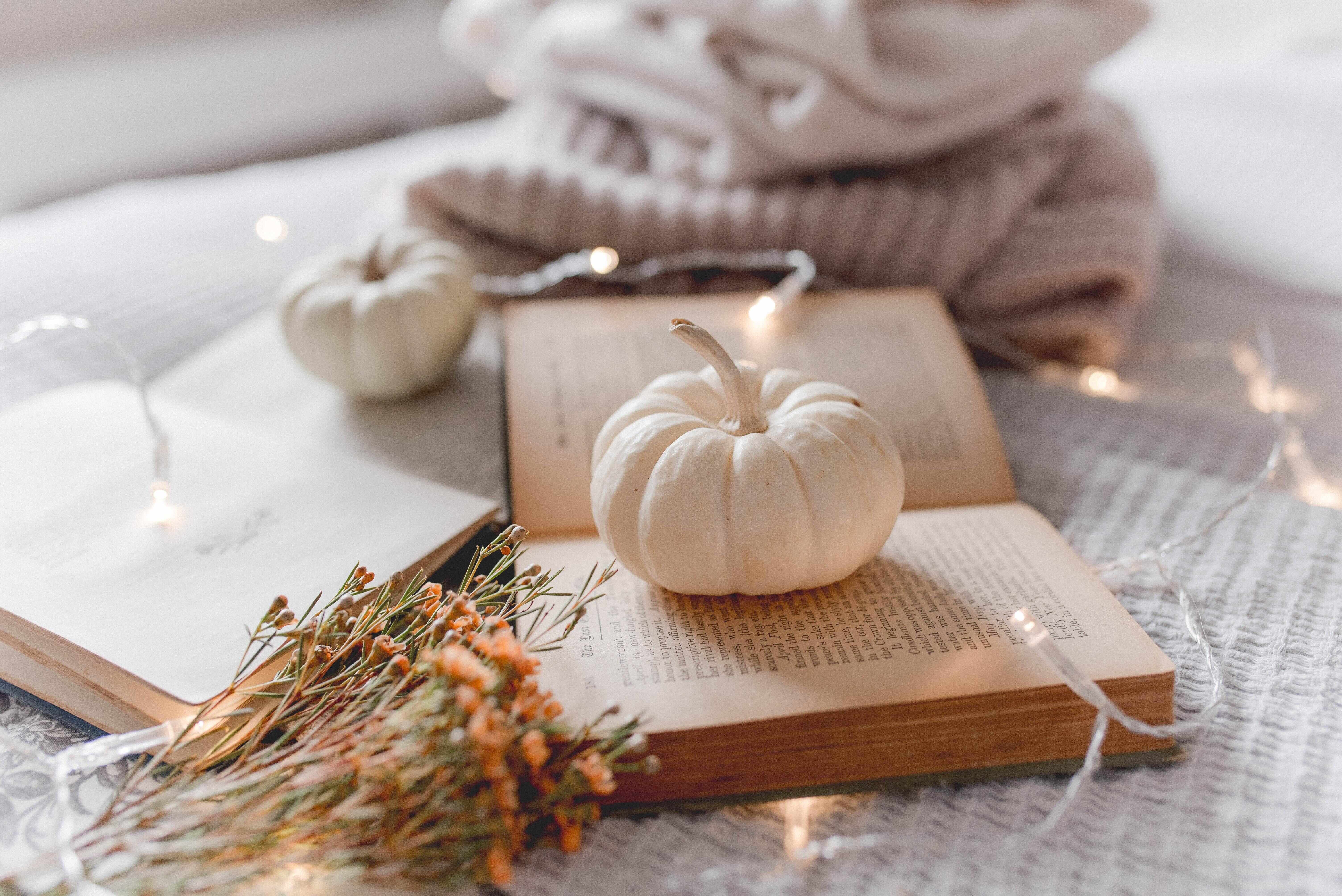 White pumpkin sitting on top of a book next to flowers