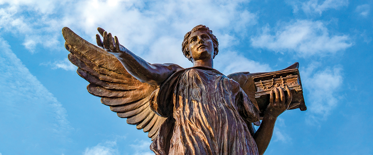 The statue of Beneficence is photographed against a bright blue sky