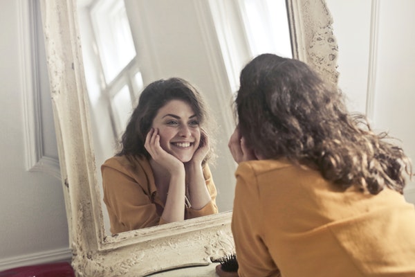 Girl looking in the mirror and smiling after getting good results with Rosacea treatment
