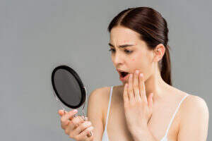 Worried woman looking at her acne in mirror.
