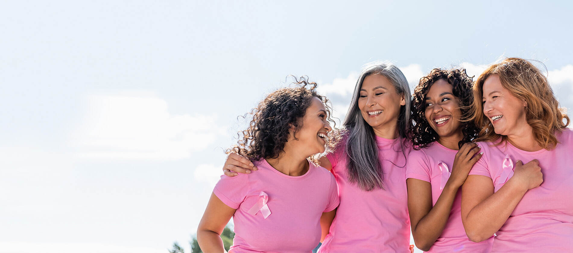 Four women smiling at each other wearing pink shirts