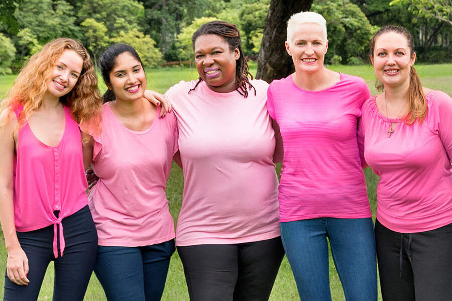 Five women wearing pink shirts interlocking arms