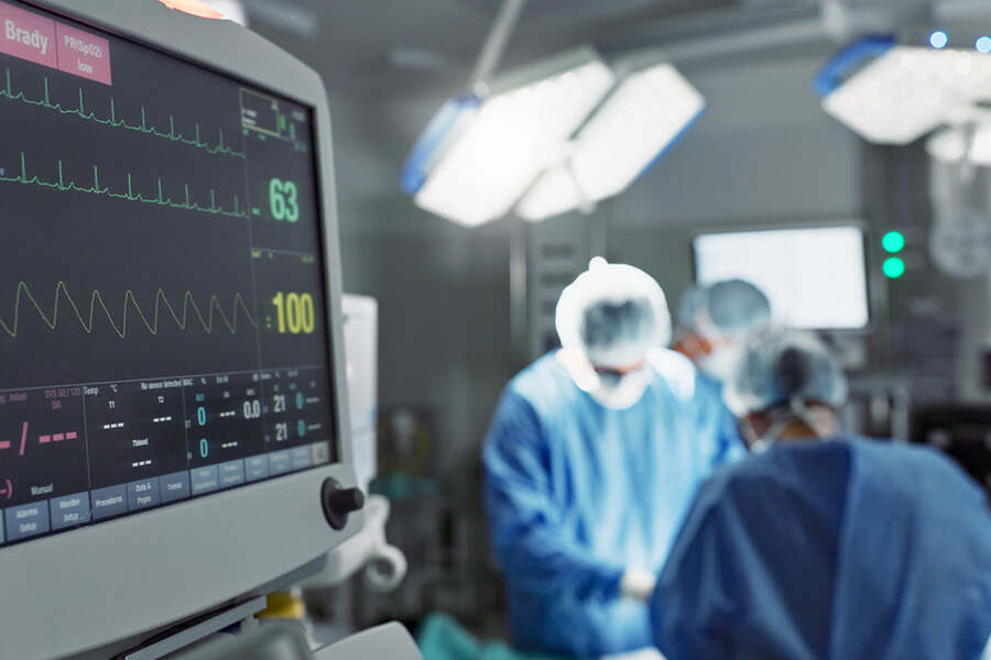 Close up of a heart monitor and doctors operation on a patient in the background 