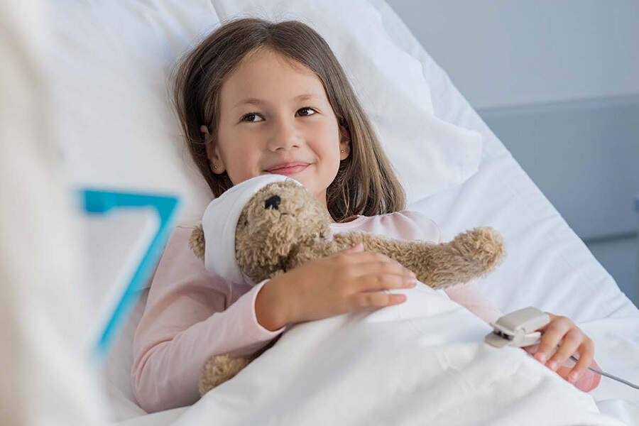 A young girl in a hospital bed holding a stuffed bear